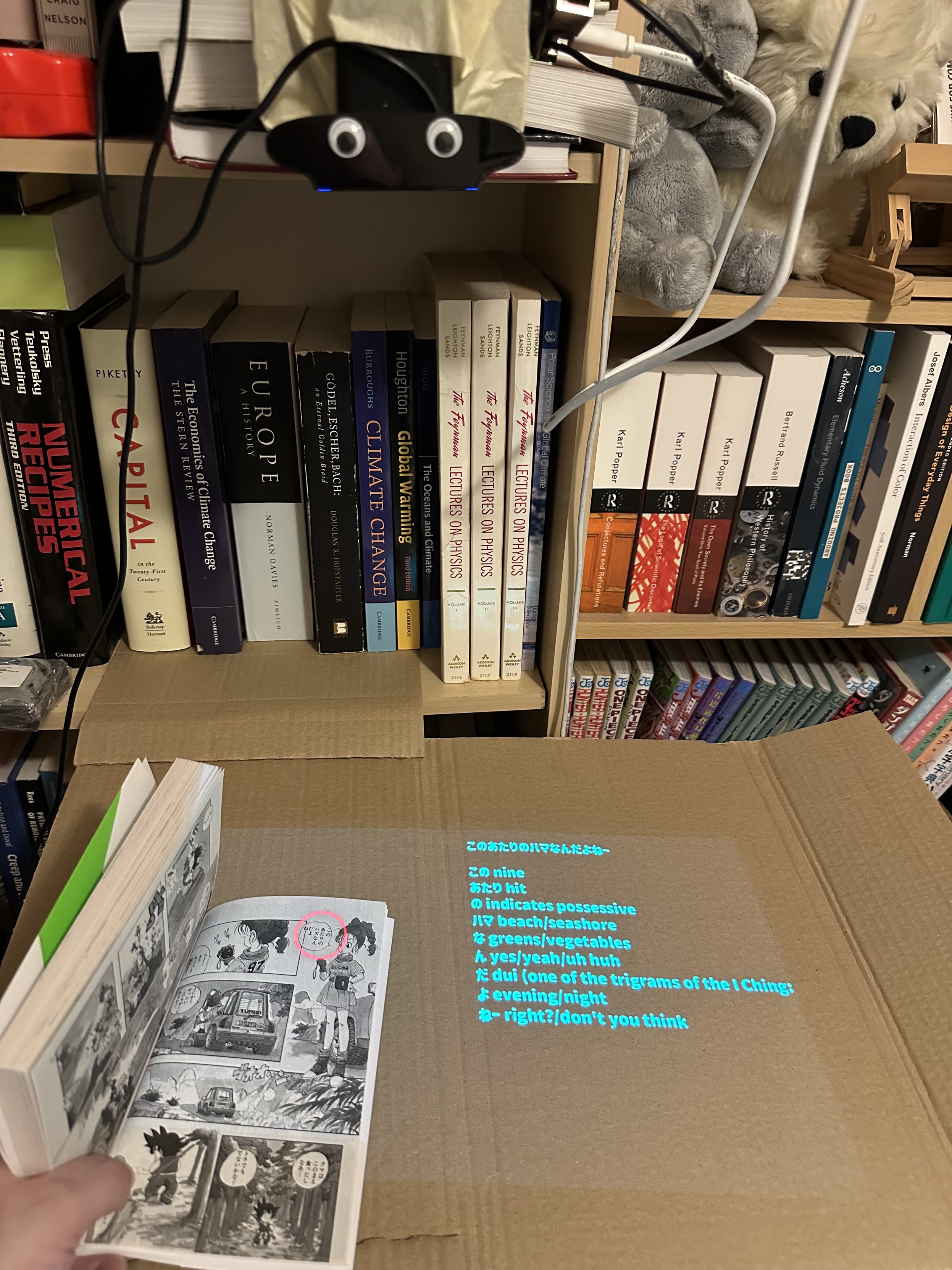 a camera and projector lined up above a volume of manga