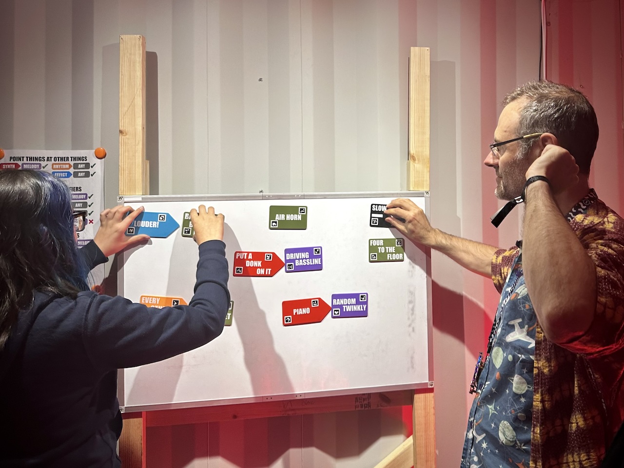 a man and a teenage girl standing in front of a whiteboard covered in colored tiles